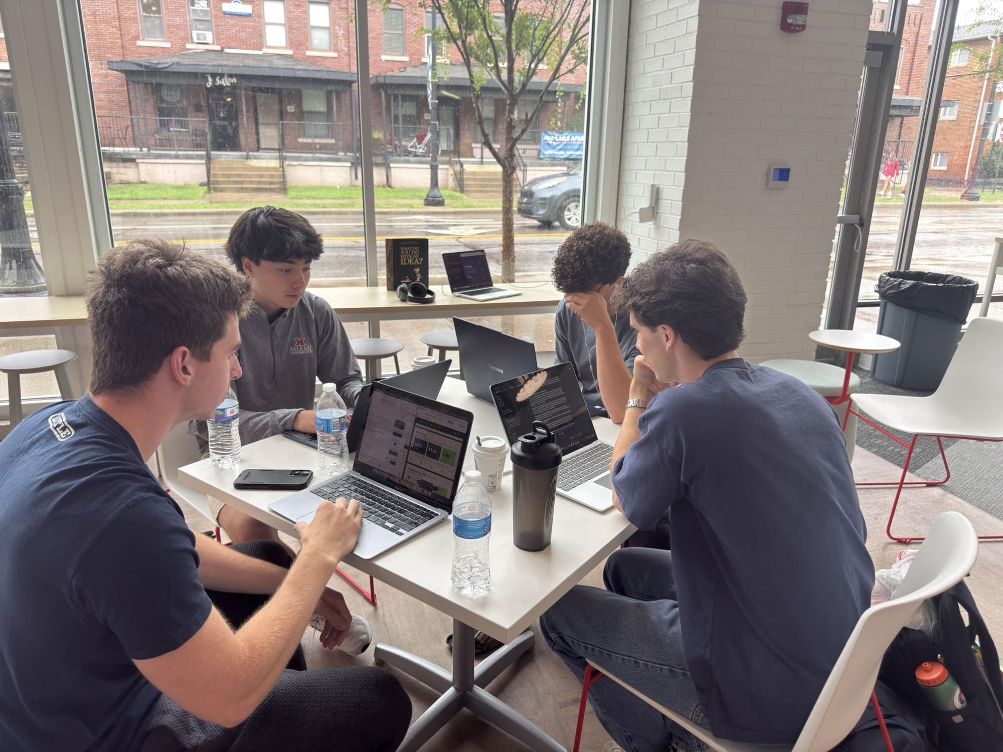 Four members building on their laptops at a table by the window during the Hackathon