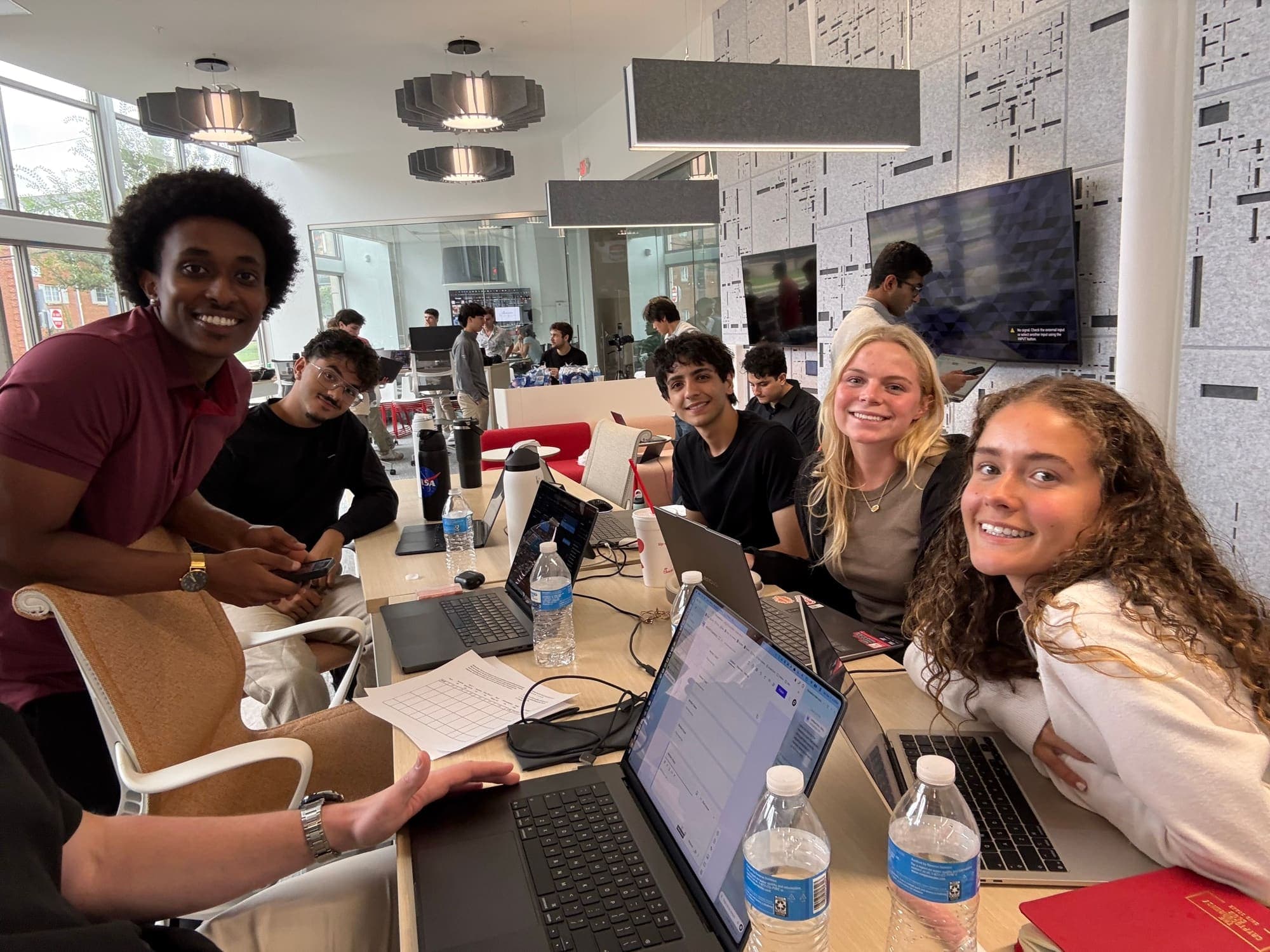 A team of Builders members smiling over their laptops at the fall 2026 Hackathon
